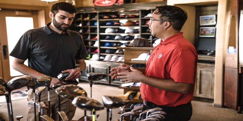 An employee helps a customer in a golfing shop with his enquiry or purchase.
