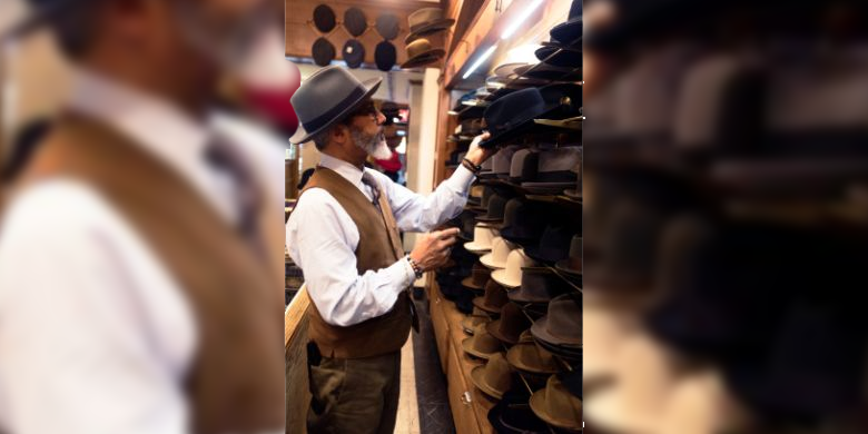 A man wearing a fedora while looking at a range of hats.