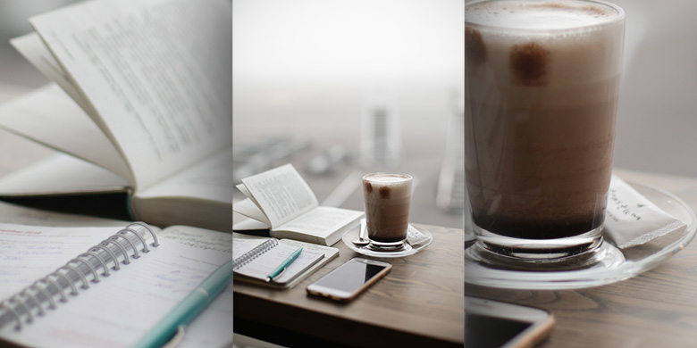 A glass of coffee sitting on a bench with an open notepad and pen.