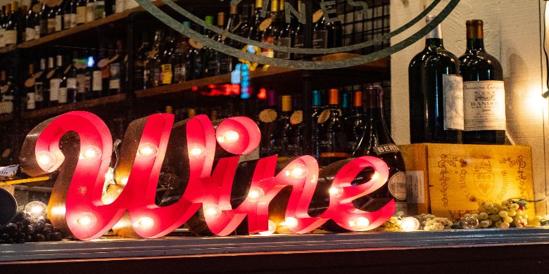 Inside a winery with a glowing retro style sign which reads 'Wine'.