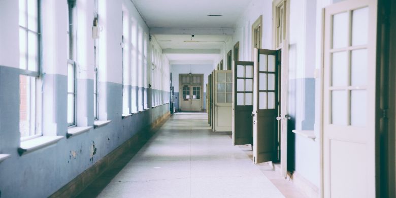 An empty school hallway with some of the classroom doors open.