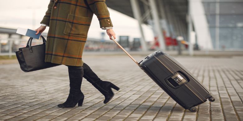 A woman carrying a purse while wheeling a suitcase around.