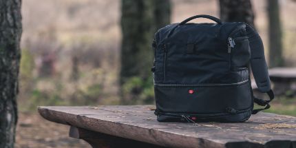 A backpack sitting on a wooden table in a forest-like location.
